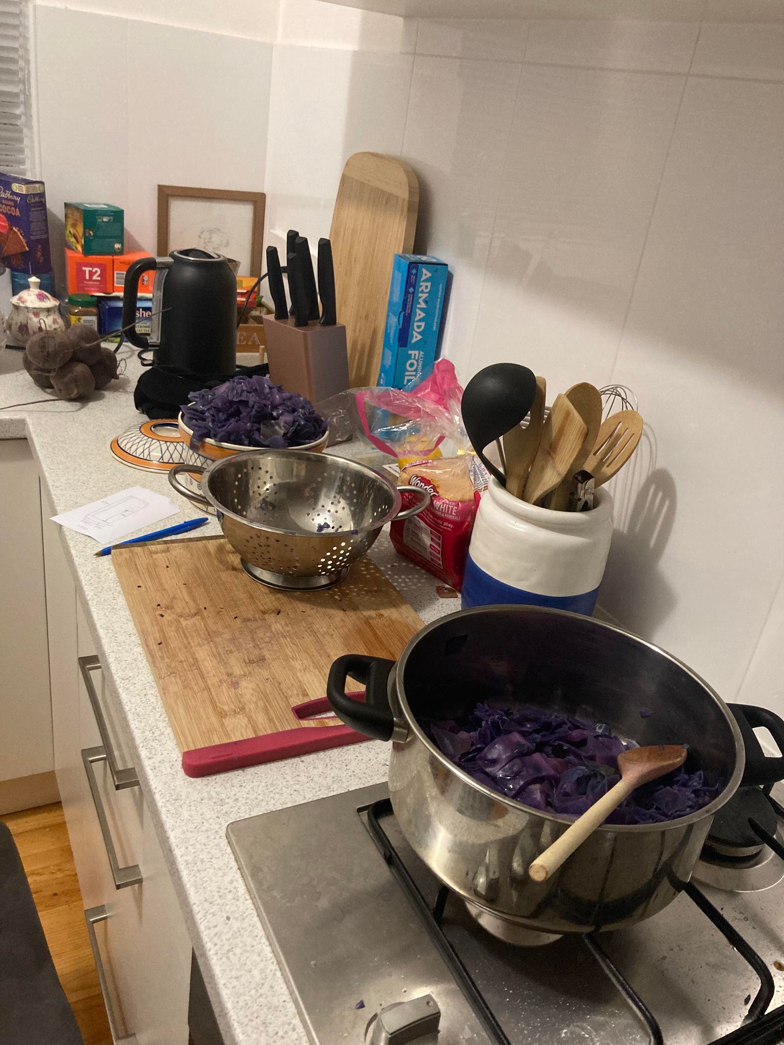 A kitchen with a strainer and a bowl and pot of boiled purple cabbage.